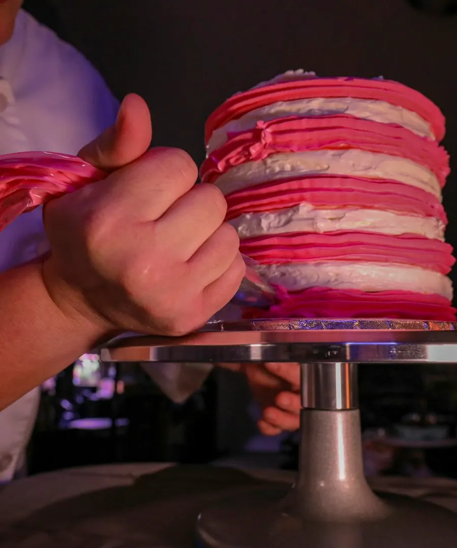 Hands decorating a layered pink cake on a turntable